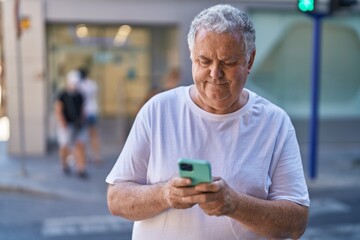 Middle age grey-haired man using smartphone with relaxed expression at street