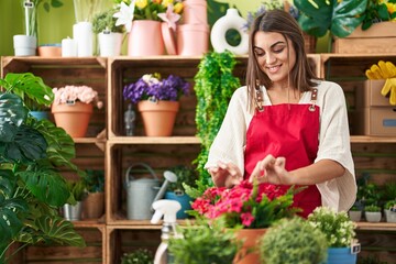 Young beautiful hispanic woman florist smiling confident touching plant at flower shop