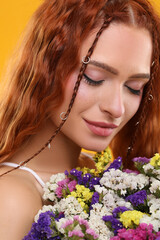 Beautiful young hippie woman with bouquet of colorful flowers on orange background, closeup