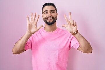 Hispanic young man standing over pink background showing and pointing up with fingers number eight while smiling confident and happy.