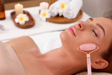 Obraz na płótnie Canvas Young woman receiving facial massage with rose quartz roller in beauty salon, closeup