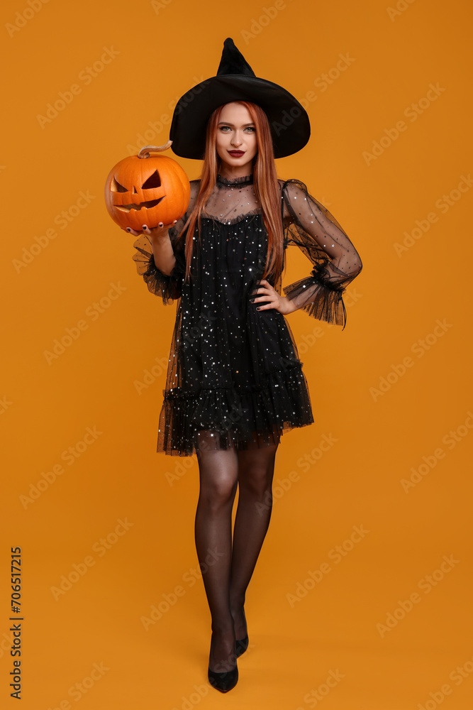 Wall mural young woman in scary witch costume with carved pumpkin on orange background. halloween celebration