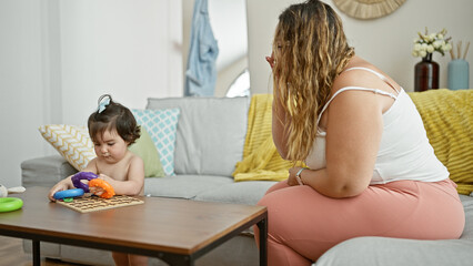 Mother and daughter enjoy a lovely day indoors, sitting on their living room sofa, playfully...