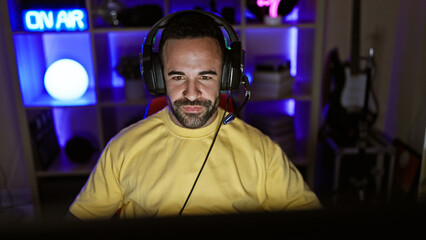 Handsome hispanic man wearing headphones in a dark gaming room at night.