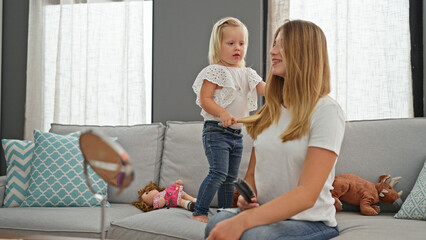 Confident caucasian mother sits comfortably, combing daughter's hair on sofa - heartwarming family...