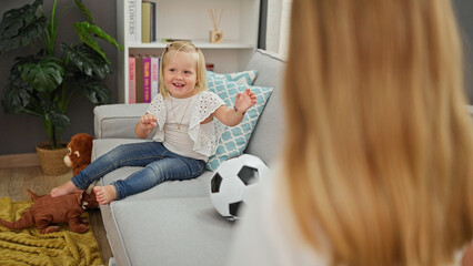 Happy caucasian mother and daughter playing ball together, sitting comfortably on living room sofa, indoors at home. smiling, relaxing family time.