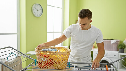 Handsome hispanic man doing laundry in a bright, modern room, placing clothes into a washing...