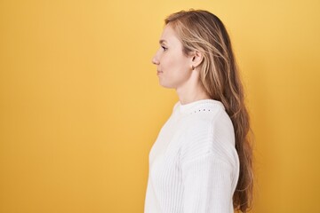 Young caucasian woman wearing white sweater over yellow background looking to side, relax profile pose with natural face and confident smile.