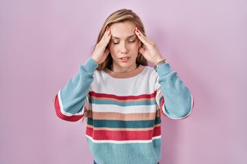 Young blonde woman standing over pink background with hand on head, headache because stress. suffering migraine.