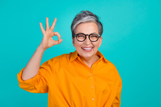 Portrait of positive senior woman demonstrating okey sign good job feedback in office for intern isolated on aquamarine color background