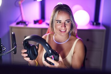 Fototapeta na wymiar Young blonde woman streamer smiling confident holding headphones at gaming room