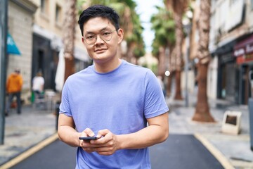 Young chinese man smiling confident using smartphone at street