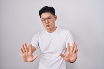 Young asian man standing over white background moving away hands palms showing refusal and denial with afraid and disgusting expression. stop and forbidden.