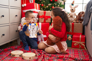Brother and sister playing with robot and monkey doll sitting on floor by christmas gifts at home