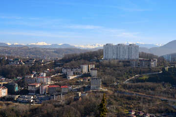 Fototapeta na wymiar Panorama of new buildings in Sochi against the backdrop of mountains covered with snow in winter