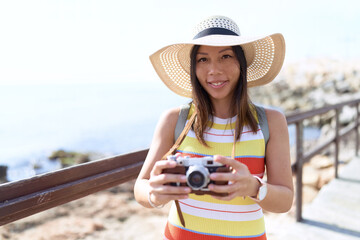 Young asian woman tourist using vintage camera at seaside