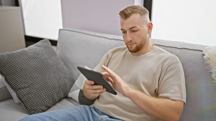 Handsome man using tablet on couch in a modern living room