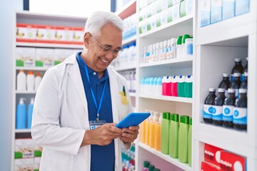 Middle age grey-haired man pharmacist using touchpad working at pharmacy - obrazy, fototapety, plakaty