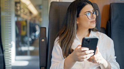 Young beautiful hispanic woman smiling using smartphone sitting inside train wagon - obrazy, fototapety, plakaty