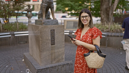 Stunningly beautiful hispanic woman in glasses, standing by iconic hachiko statue on bustling tokyo...