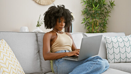 African american woman using laptop sitting on sofa at home