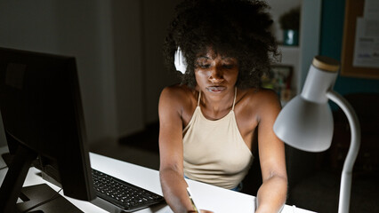 African american woman business worker using computer and headphones taking notes at the office