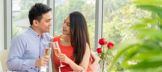 Happy Asian couple holding glass of champagne talking and smiling together. man and woman flirtng on dating on Valentine's day or anniversary at a restaurant. love and togetherness