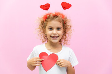 Beautiful little girl with paper red heart shaped greeting card. Portrait of child on pink. Paper...