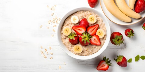Bowl of oatmeal porridge with strawberry and banana on white table top view. Healthy and diet breakfast. - obrazy, fototapety, plakaty