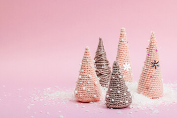 Handmade winter composition. Set of crocheted Christmas trees, artificial snow on pink background