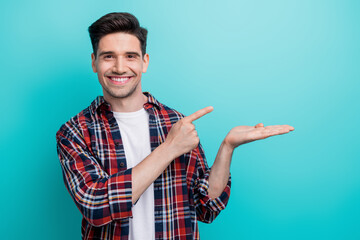 Photo of cheerful funky man dressed plaid shirt holding arm showing finger empty space isolated...
