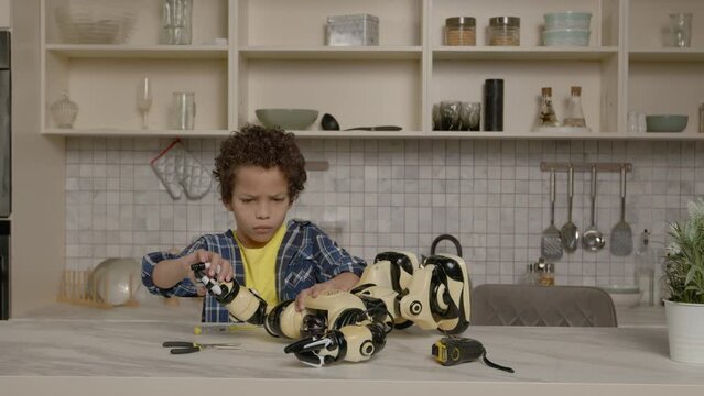 Skillful concentrated smart cute preadolescent boy, fixing broken toy using work tools, checking functions and features of damaged robot after repair while spending time indoors.