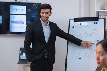 A South Asian man in a business suit points to growth charts during a dynamic corporate strategy...