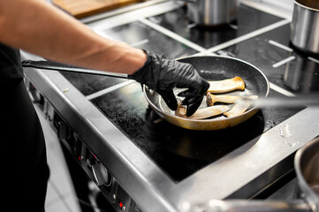Professional chef cooking mushroom in frying pan on stove in restaurant kitchen