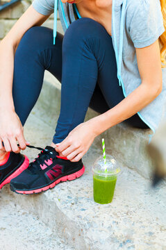 Green detox smoothie cup and woman lacing running shoes before workout © Dasha Petrenko