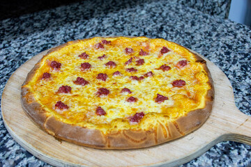 Close-up of a delicious Italian pizza with cheese and sausages (Merguez) on a cutting board.