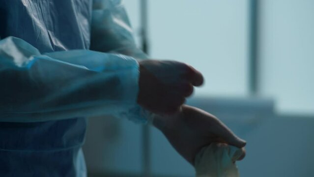 Close-up unrecognizable male doctor hands takes off gloves after successful surgical operation in dark operation room. Closeup of paramedic removes latex gloves after working. Shooting in slow motion.