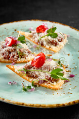 Elegant beef tartare on crispy toasts with parmesan, greens, and tomatoes on a speckled turquoise plate