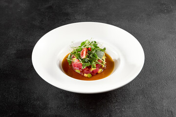 Tuna and avocado tartare topped with microgreens and cherry tomatoes, served in a white bowl