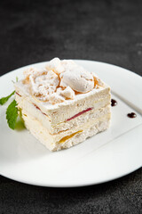 Delicate meringue cake with creamy cheese filling, garnished with a sprig of mint on a white plate