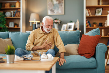Senior man sitting on sofa at home with sickness
