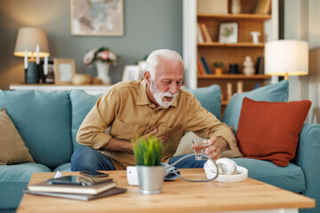 Senior man sitting on sofa at home with sickness