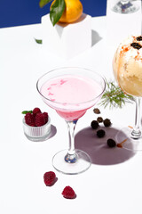 A delicate raspberry margarita cocktail, accented with fresh raspberries and pine cone decor on a geometric white stand