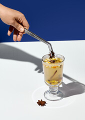 A hand adorns white mulled wine with spices, creating a cozy and aromatic winter drink against a contrasting background