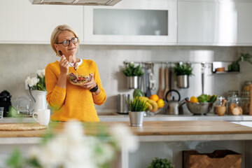 Attractive mature woman eating salads in her kitchen
