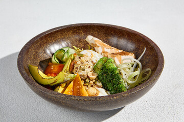 A bowl with grilled chicken, avocado, and mixed vegetables, served in a rustic bowl