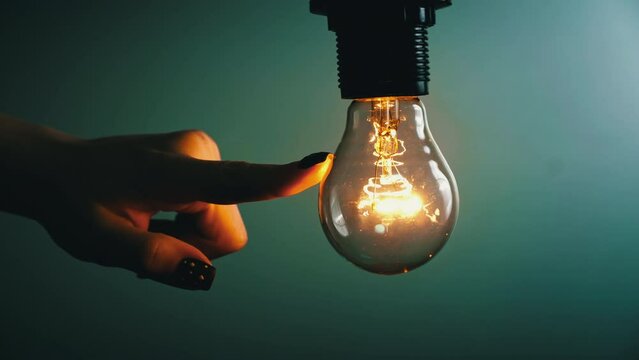 Light Bulb Turns On And Goes Out At The Touch Of A Person's Hand In The Dark. Slow Turning On And Off Of A Tungsten Light Bulb. Filament Of A Blinking Vintage Light Bulb. Energy, Electricity, Light