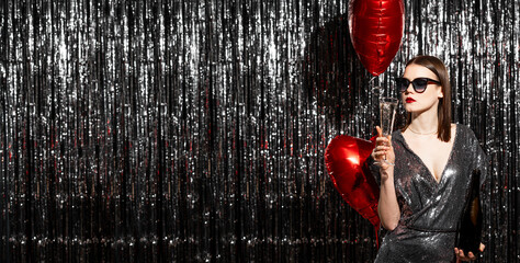 Elegant young Woman on Valentines Day party is wearing sequin silver dress and is posing on tinsel...