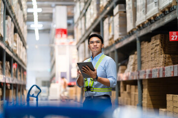 warehouse worker in a blue security suit uses a digital tablet to inspect inventory in a large...