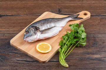 Fresh dorado fish with lemon and cilantro on a wooden cutting board.